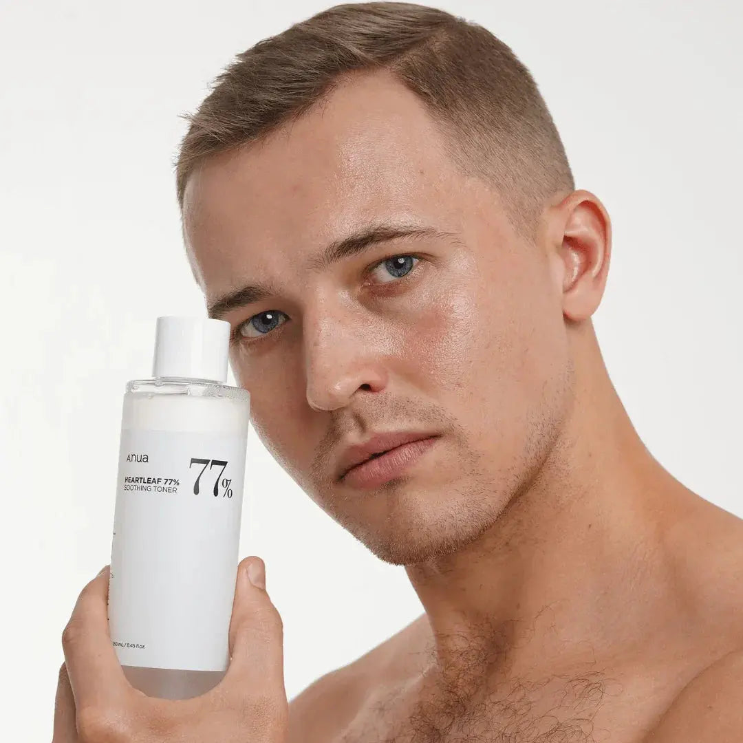 Man håller en vit flaska Anua Heartleaf 77% Soothing Toner intill ansiktet mot vit bakgrund