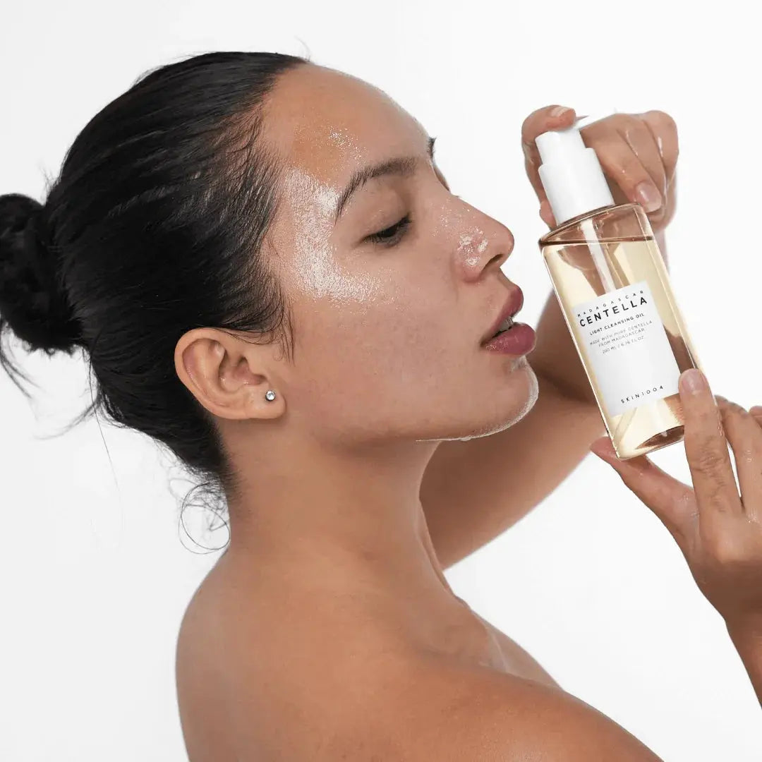 Kvinna med olja i ansiktet håller en pumpflaska SKIN1004 Centella Light Cleansing Oil nära kinden
