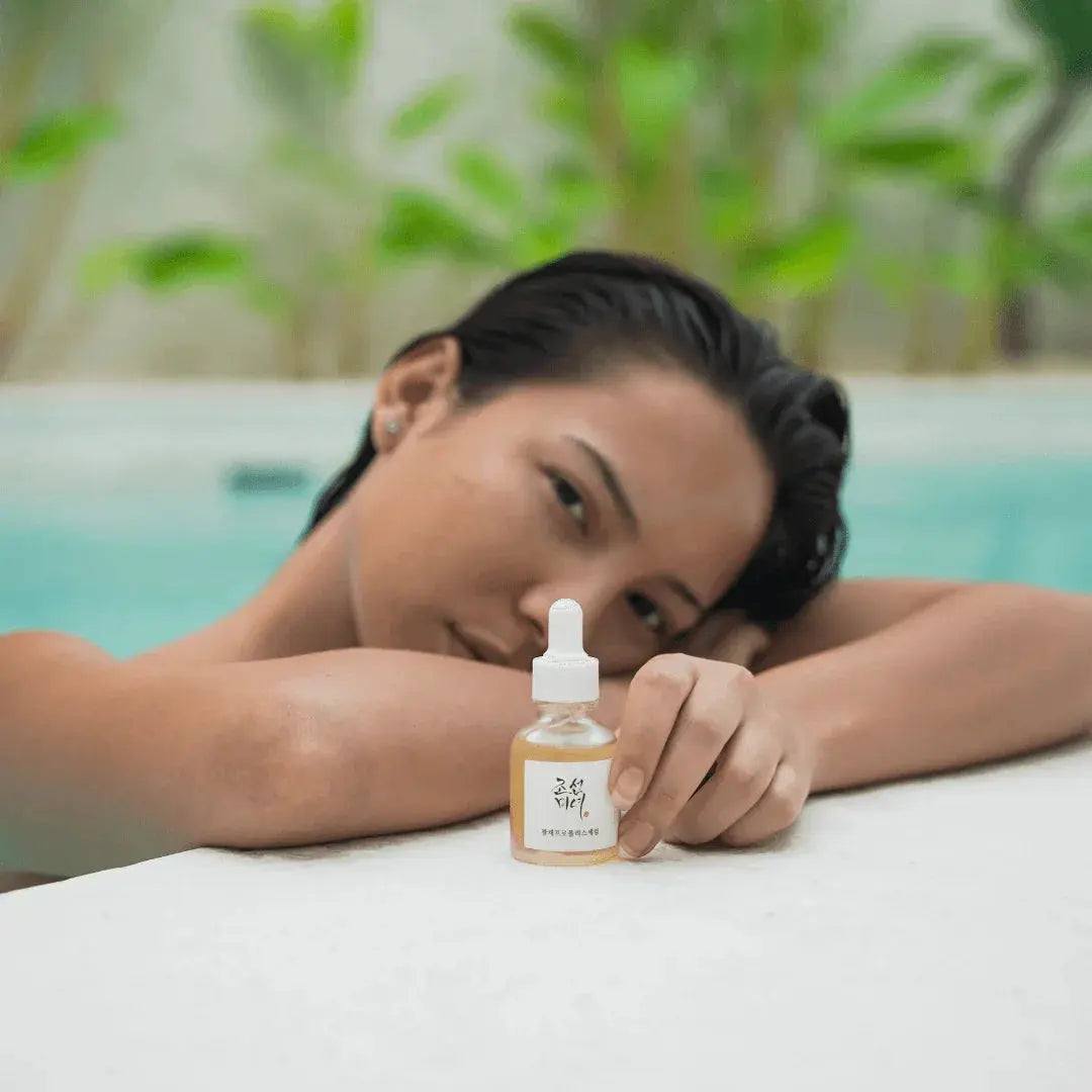 Frau stützt die Arme auf den Beckenrand und hält eine kleine bernsteinfarbene Pipettenflasche Beauty of Joseon Serum