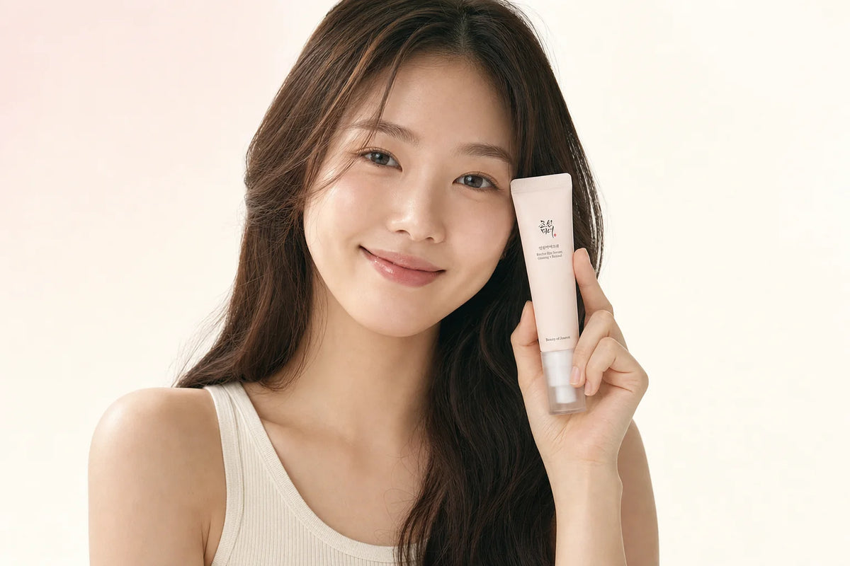 Smiling woman with long hair holding a light pink Beauty of Joseon skincare tube against a soft cream background