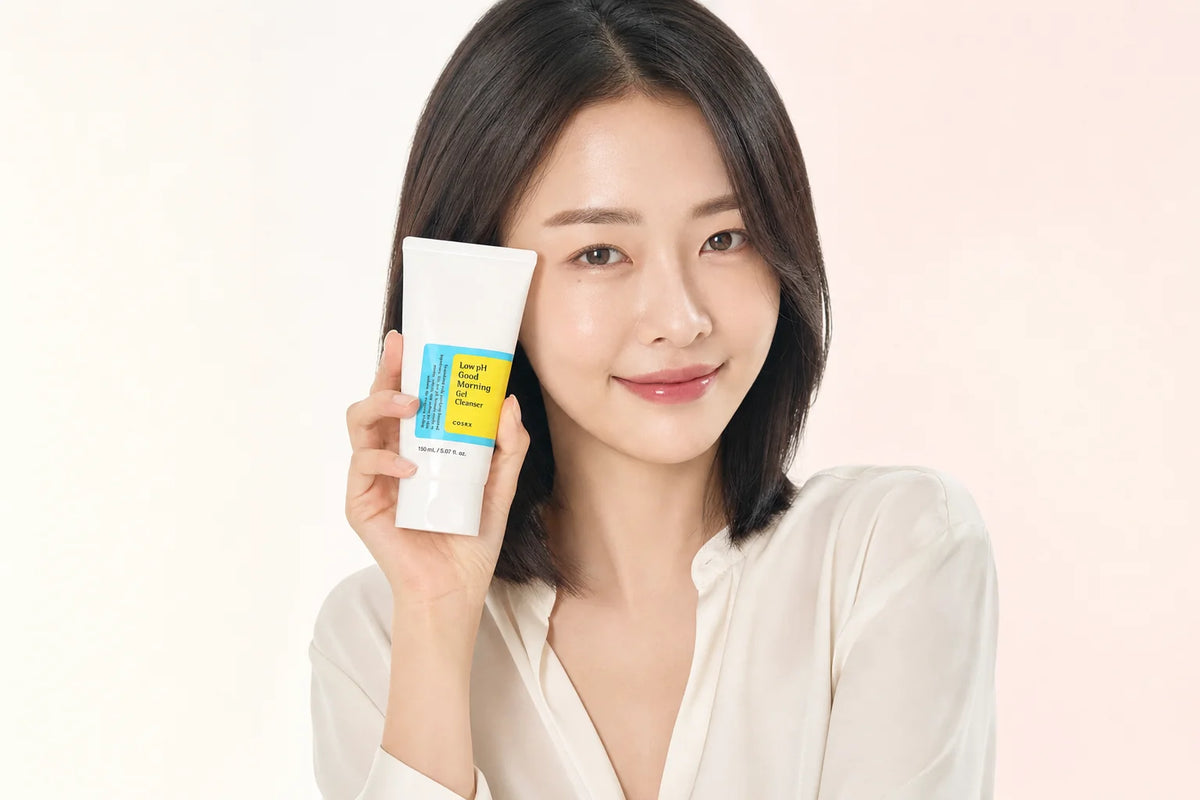 Woman in a white blouse holding a COSRX Low pH Good Morning Gel Cleanser tube beside her face
