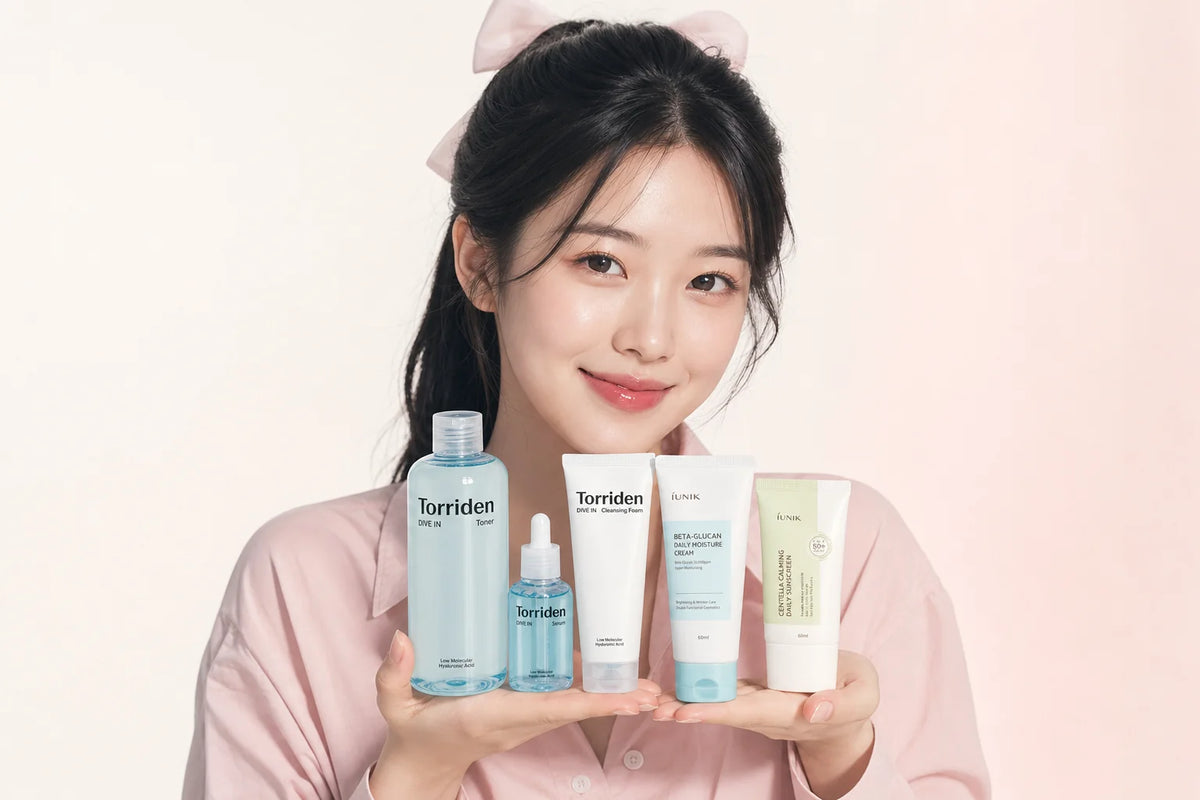 Woman with a pink hair bow presenting five Torriden and iUNIK toner, serum, cleanser and cream products